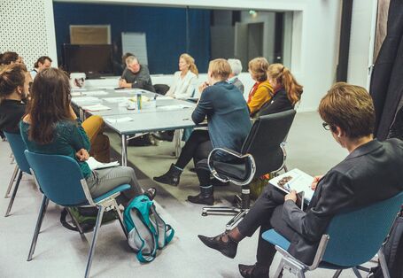 Gruppe von diskutierenden Teilnehmern im Hintergrund, schräg davor eine weitere Person