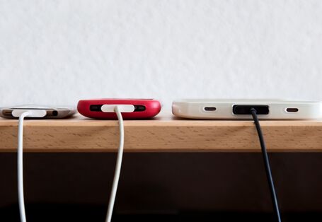 Drei Smartphones werden gleichzeitig über ihre Ladegeräte mit Strom geladen. 