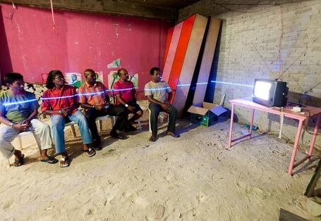 Eine Gruppe von Männern die fernsehn guckt. Das Kunstprojekt zeigt, dass bei gestiegenem Wasserpegel bis zur Brust unter Wasser sitzen würden.