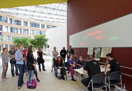 Vier Personen sitzen an einem Tisch, darum Ausstellungsbesucher