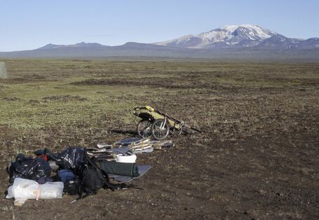 Eine weite Steppenlandschaft, im Hintergrund schneebedeckte Berge. Im Vordergrund der Handwagen der Künstlerin mit ihrem Gepäck.