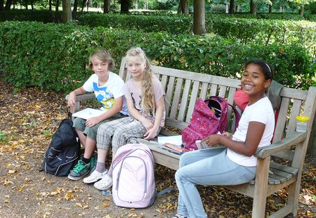 Drei Kinder sitzen auf einer Bank im Freien und malen, lachen