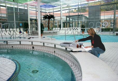 Eine Frau entnimmt in einem öffentlichen Hallenbad eine Wasserprobe aus einem Schwimmbecken.