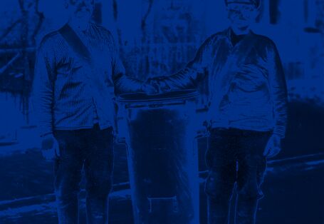 Zwei Männer tragen einen großen Standeimer