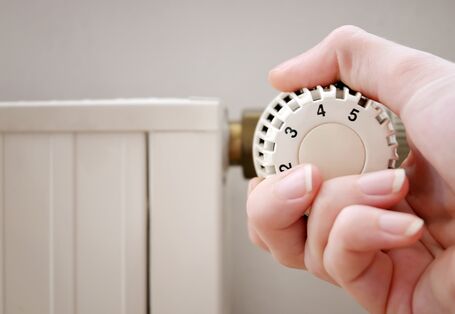 Nahaufnahme: Eine Hand dreht das Thermostat einer Heizung auf.