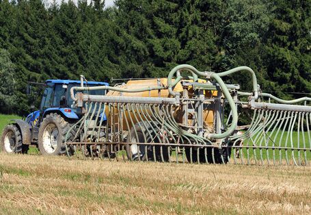 Ein Traktor bringt Gülle auf einem Feld aus. Dafür nutzt er einen Aufsatz mit sogenannten Schleppschläuchen, die dafür sorgen, dass die Gülle nah über dem Boden ausgebracht wird.