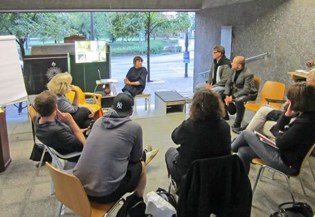 Diskussionsrunde im utopischen Institut: 9 Personen sitzen in einem Stuhlkreis
