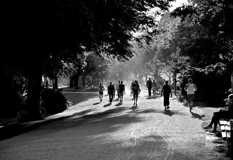 Schwarz-weiß-Aufnahme eines Parks, in dem viele Menschen joggen, spazierengehen oder auf einer Bank sitzen.