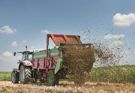 Ein Taktor mit Hänger verteilt Dünger auf einem Feld