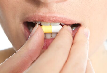 Das Bild zeigt den Mund einer Frau. Mit ihrer rechten Hand führt sie eine Tablette an ihren Mund. 