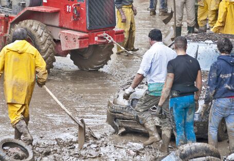 Männer räumen mit Schaufeln und Bagger den Schlamm nach dem Hochwasser weg
