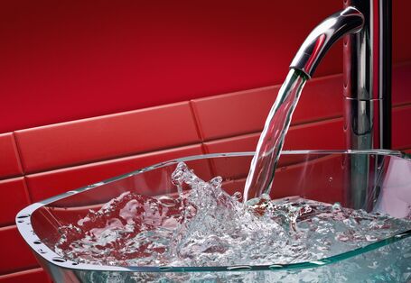 Trinkwasser fließt aus einem Wasserhahn in ein Becken aus Glas