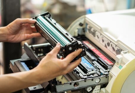 Jemand hält eine Tonerkartusche vor einem Druckgerät in der Hand