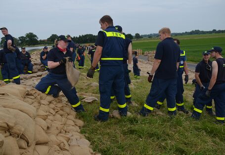 Personen des THW beim Errichten eines Deichs aus Sandsäcken in Flußlandschaft.