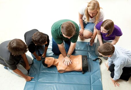 Jugendliche üben Herzmassage am Torso einer Übungspuppe im Erste Hilfe Kurs .