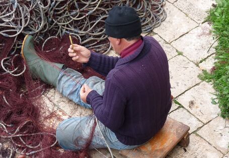 Rückenaufnahme eines Fischers, der Netze repariert.