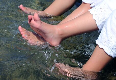Füße von zwei Mädchen in weißen Kleidern in Wasserbecken.