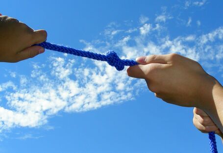 Blaues Seil mit Knoten an dem von Händen in verschiedene Richtungen gezogen wird.