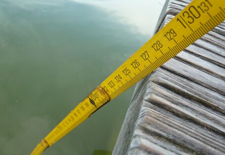 Nahaufnahme gelber Zollstock, der von einem Bootssteg ins Wasser reicht.