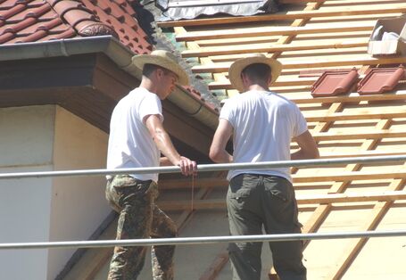 Zwei Männer mit Strohhüten auf Baugerüst beim Decken eines Daches.
