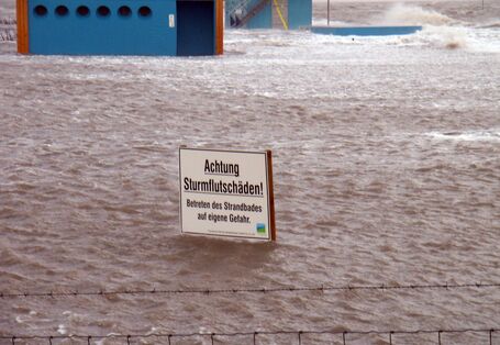 Warnschild vor Sturmflutschäden in überfluteter Hafenanlage.