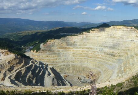 Vorne ist ein Steinbruch zu sehen, dahinter Hügel und blauer Himmel mit einigen Wolken.
