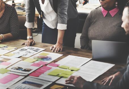 Menschen stehen an einem Arbeitstisch mit Papieren.