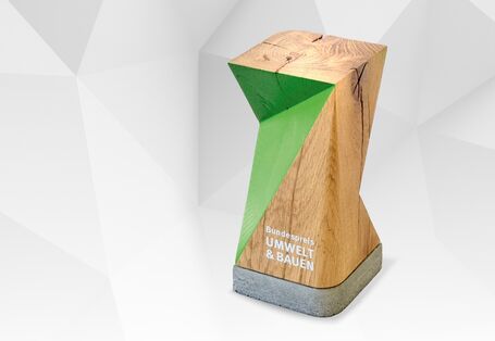 Schriftzug "Bundespreis Umwelt & Bauen" und Bild einer Trophäe aus Holz
