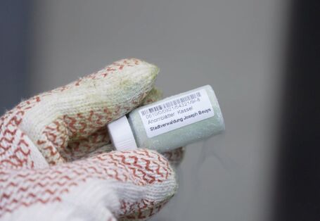 Hand mit Handschuh hält eine Probe in einem kleinen Fläschchen.