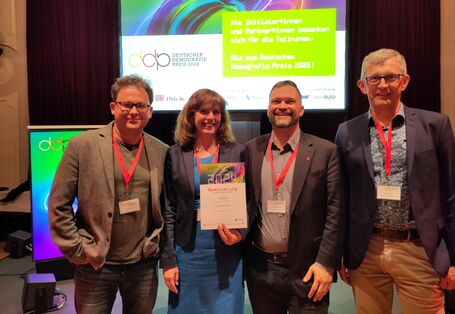 Vier Personen stehen nebeneinander und lächeln in die Kamera