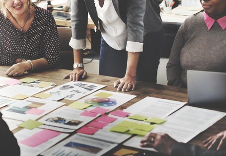 Teamsitzung, auf dem Tisch sind viele Unterlagen und bunte Klebezettel verteilt