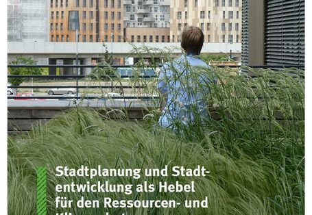 Mensch sitzt in hohem Gras und schaut auf eine Baustelle in der Stadt