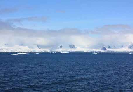 Eine weiße Wolkenschicht umgibt antarktische Berge an der Küste. Darüber sieht man eine zweite dunkler und dünnere Wolkenschicht. 