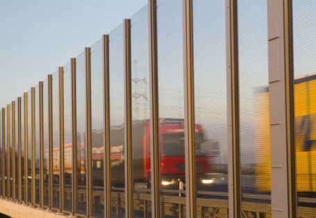 Lkws fahren auf der Autobahn hinter einer Lärmschutzwand.