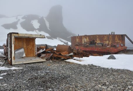 Auf einem Strandabschnitt liegt rostiger Schrott. Im Hintergrund erhebt sich ein Berg, der von Nebel verhüllt wird.