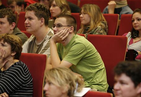 Blick auf das Publikum. Ein Schüler und eine Lehrerin hören interessiert zu, das Gesicht in die Hände gestützt.