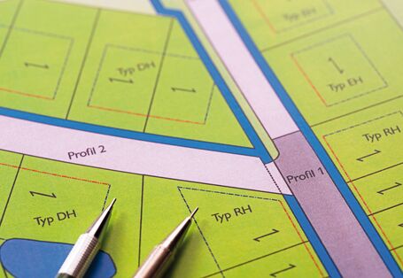 The picture shows an excerpt from a development plan for a residential area with semi-detached and terraced housing. There are two mechanical pencils lying on the plan.