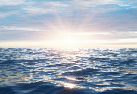 Das Bild zeigt eine leicht bewegte Meeresoberfläche bei tiefstehender Sonne. Der Himmel ist von bläulich-grauen Wolken verhangen.