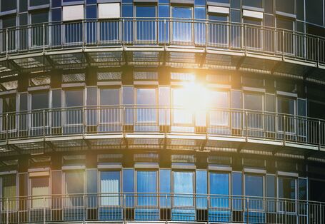 The picture shows the glass frontage of a house reflecting the sun. Some of the windows are part-shaded by means of external roller shutters.