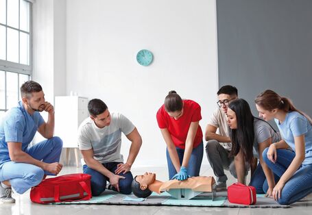 Das Bild zeigt eine Gruppe von zwei Frauen und zwei Männern bei einer Erste-Hilfe-Übung. Die Kursleiterin zeigt an einer Puppe die Herzdruckmassage.