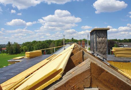 Das Bild zeigt einen abfedeckten Dachstuhl, auf dessen linker Seite Dämmmaterial verlegt wurde.