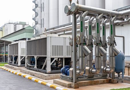 Das Bild zeigt ein Rohrleitungssystem vor industriellen Anlagen zur Einspeisung von Kaltwasser in einen Produktionsprozess. Neben den Rohren sind weitere technische Aggregate zu sehen.