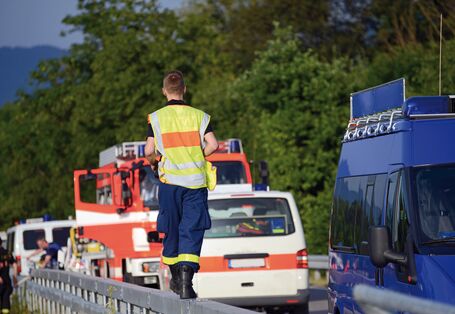 Das Bild zeigt drei Einsatzfahrzeuge der Feuerwehr und des Technischen Hilfswerks, die auf einer Überlandstraße stehen, darunter ein Löschgruppenfahrzeug. Ein Mann mit Warnweste und Einsatzhose des THW läuft auf der Mittelleitplanke.