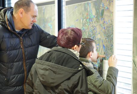 Familie schaut sich eine Landkarte an und der Vater zeigt seinem Sohn und seiner Ehefrau etwas auf der Karte, die aus der Luft fotografiert wurde und farbig markierte Bereiche hat