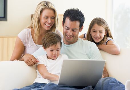 Familie sitzt auf dem Sofa und schaut zusammen auf den geöffneten Laptop