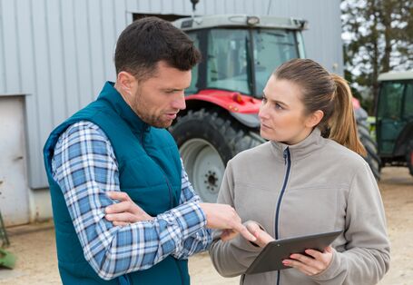 Das Bild zeigt eine Landwirtin und einen Landwirt auf einem Hof mit einem Tablet und diskutieren eine Entscheidung für den Landwirtschaftsbetrieb.