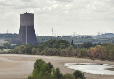 Das Bild zeigt ein nahezu trockengefallenes Flussbett, das von Baumreihen gesäumt ist. Im nahen Hintergrund erhebt sich ein Kühlturm. 