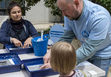 Gäste und Standbetreuer mit Altpapier, Wasser und Formen mit dem Umweltzeichen Blauer Engel, um daraus einen Engel zu schöpfen. 