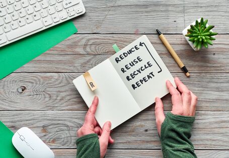 Ein Bild mit einem Notizbuch auf dem Wörter geschrieben sind. Diese lauten reduce, reuse, recycle, repeat. Auf deutsch: reduzieren, wiederverwenden, recyceln, wiederholen. 