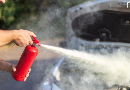Ein Feuerwehrmann hält den Schlauch, aus dem Schaumlöschmittel quillt, im Hintergrund ist Feuer